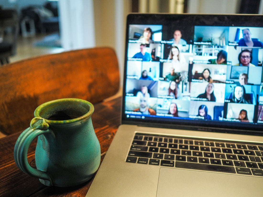 Laptop auf einem Schreibtisch zeigt eine Videokonferenz mit mehreren Teilnehmenden, daneben eine Kaffeetasse